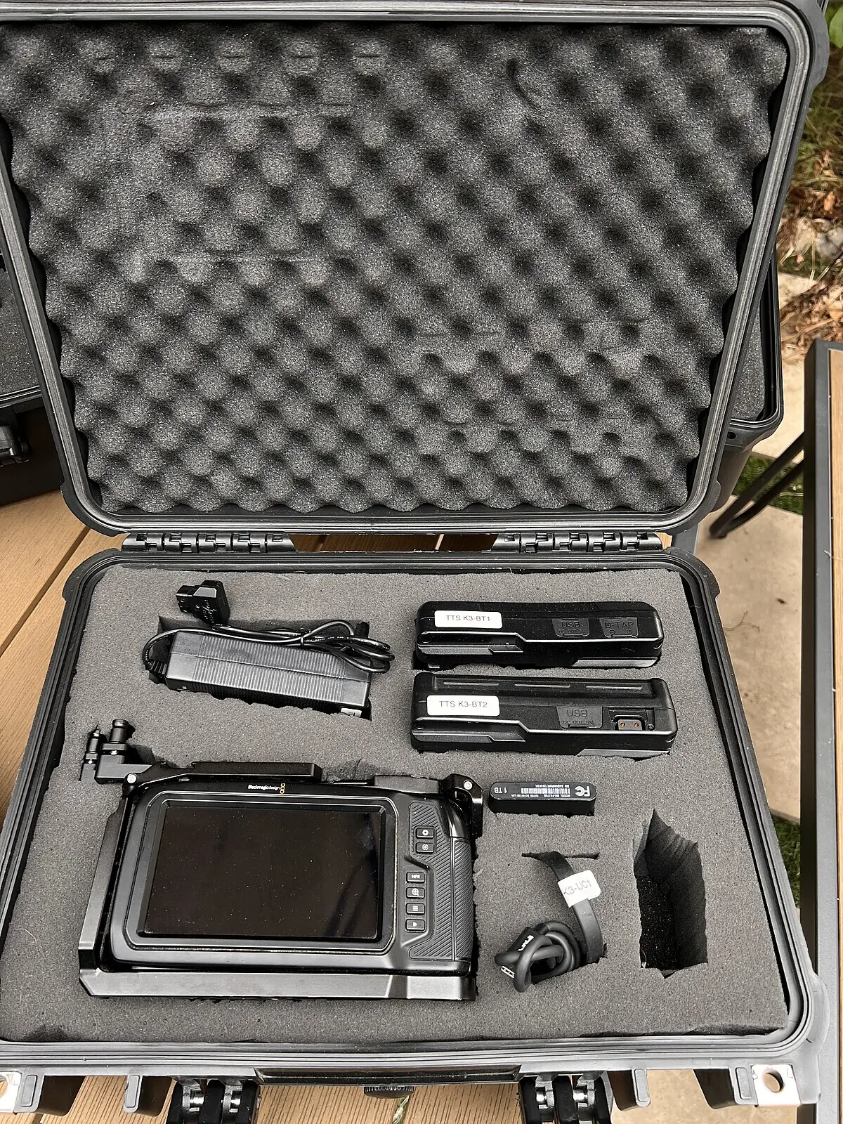 An open kit case: Blackmagic 6K camera in its cage, two V-mount batteries, SSD, charger and cables