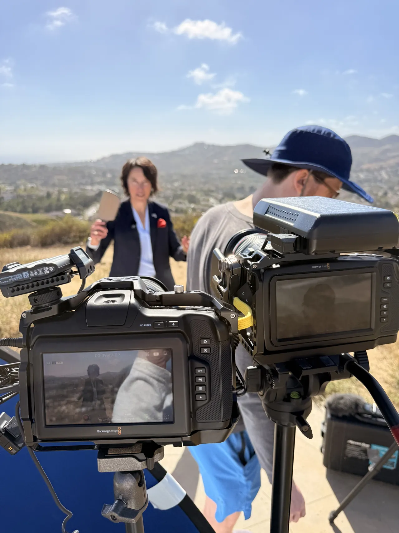 Two cameras on tripods filming an outdoor interview on a hillside